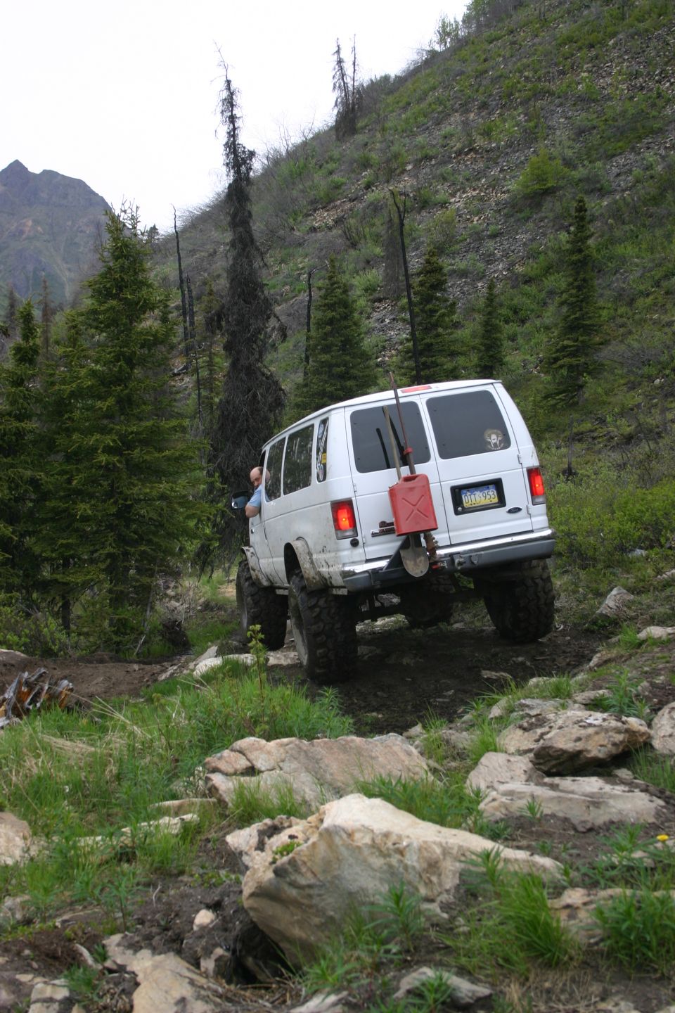 White van with red gas can and shovel on rear, driving off-road