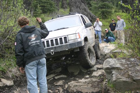 2003 Jeep TJ - A silver Jeep Grand Cherokee navigates a challenging rocky terrain with onlookers observing the off-road adventure.
