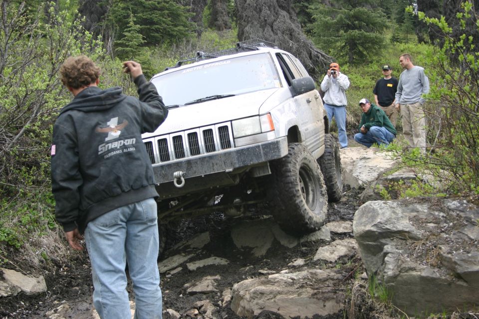 Silver Jeep Grand Cherokee off-roading on a rocky trail, front-left tire elevated