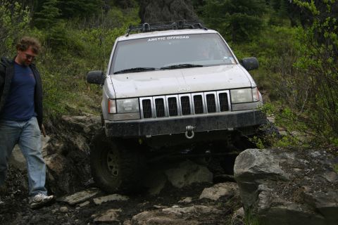 2003 Jeep TJ - A Jeep Grand Cherokee tackles a challenging off-road trail with large rocks and mud.
