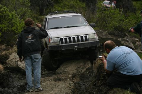 2003 Jeep TJ - A silver Jeep Grand Cherokee tackles a challenging rocky trail, with spectators observing and photographing the off-road event.