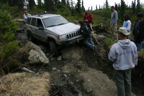 2003 Jeep TJ - A group of people help push a silver Jeep Grand Cherokee through a challenging off-road obstacle.