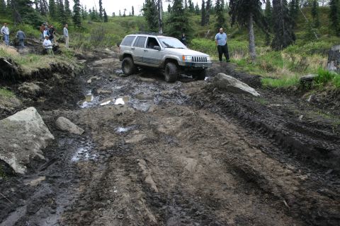 2003 Jeep TJ - Silver Jeep Grand Cherokee tackles a challenging muddy and rocky off-road path.