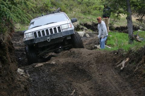 2003 Jeep TJ - A silver Jeep Grand Cherokee navigates a challenging muddy off-road course with two people observing.