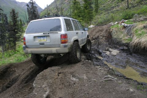 2003 Jeep TJ - Jeep Grand Cherokee tackling a difficult muddy path in a mountainous, wooded area.