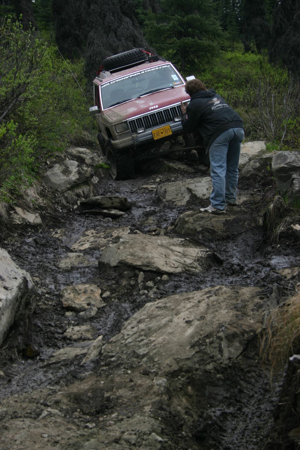 Red Jeep Cherokee XJ on rocky trail, person guiding