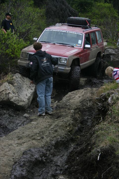2003 Jeep TJ - A red Jeep Cherokee XJ is shown attempting to traverse a difficult off-road course with onlookers present.
