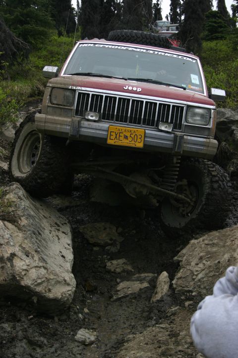 2003 Jeep TJ - A red Jeep Cherokee XJ navigates a challenging rocky trail, with another vehicle visible in the background.