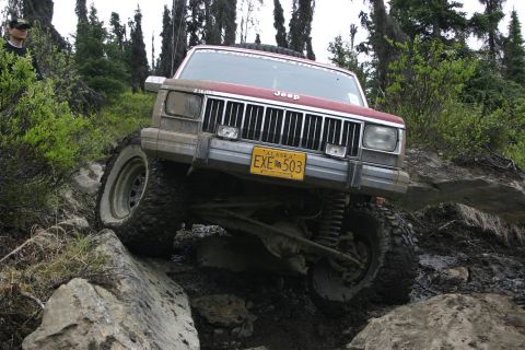 2003 Jeep TJ - A red Jeep Cherokee XJ navigates a challenging rocky and muddy trail during an off-road event.