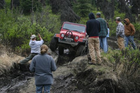 2003 Jeep TJ - A red 2003 Jeep TJ is shown tackling a challenging muddy obstacle during an off-road event.