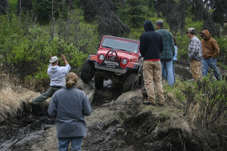 Red 2003 Jeep TJ navigating a difficult muddy off-road trail with several people watching