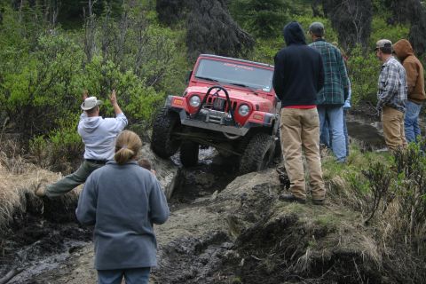 2003 Jeep TJ - A group of people watch as a red Jeep Wrangler navigates a difficult off-road obstacle.
