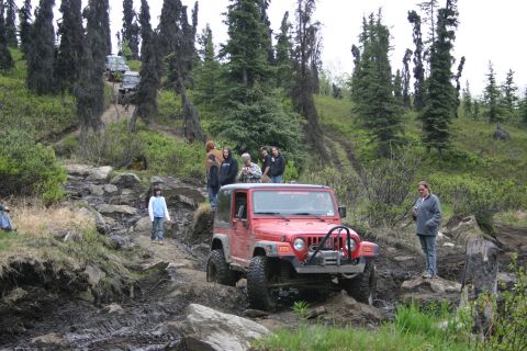 2003 Jeep TJ - A group of people watch a red Jeep Wrangler navigate a challenging off-road course.
