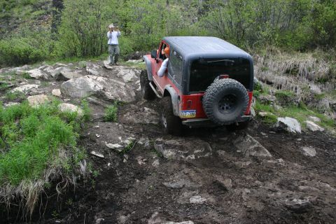 2003 Jeep TJ - A red Jeep Wrangler navigates a challenging off-road course with a person observing in the background.
