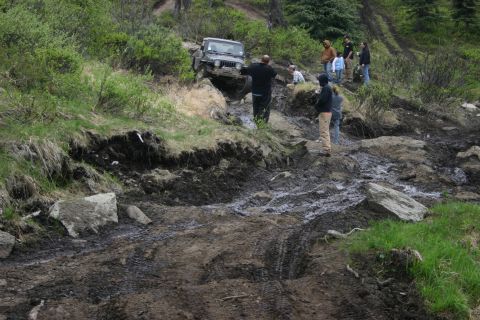 2003 Jeep TJ - A group of people observe a Jeep Wrangler as it attempts to climb a difficult, muddy, and rocky off-road path.