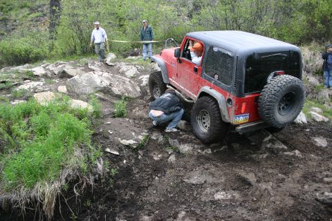 2003 Jeep TJ - A red 2003 Jeep TJ tackles a challenging off-road trail with muddy terrain and large rocks.