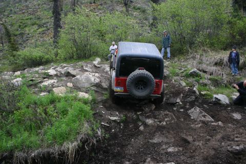 2003 Jeep TJ - A red Jeep Wrangler tackles a challenging off-road trail, with onlookers observing the difficult terrain.