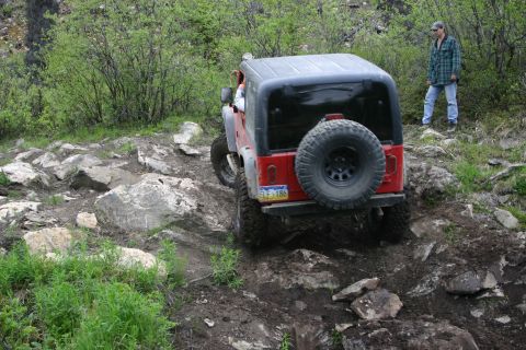 2003 Jeep TJ - Red Jeep TJ tackling a challenging rocky trail, with a person observing from the side.