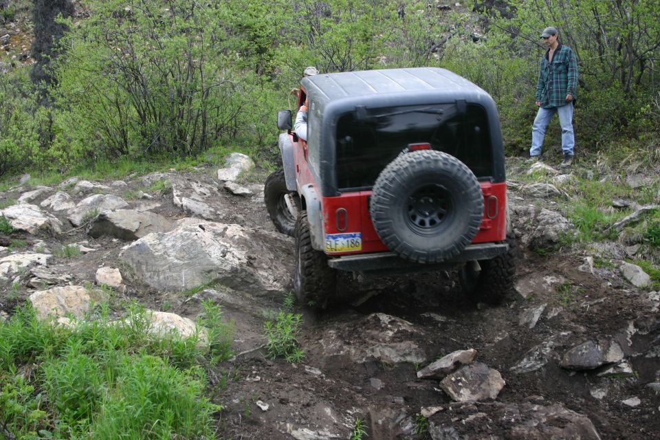 2003 Jeep TJ navigating a rocky off-road trail with a person standing nearby