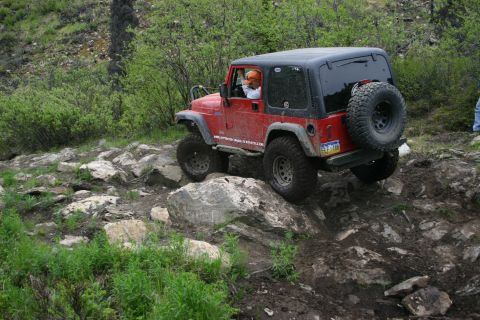 2003 Jeep TJ - A red Jeep Wrangler navigates a rocky off-road trail, demonstrating its capability on challenging terrain.