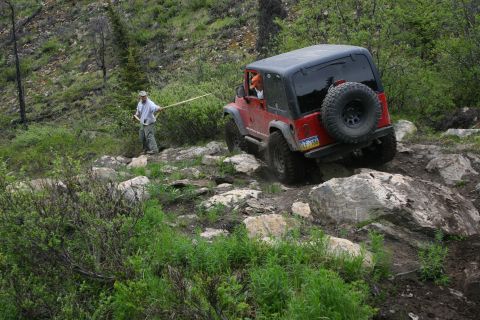 2003 Jeep TJ - A red Jeep Wrangler TJ tackles a challenging rocky off-road course, with a companion offering guidance.