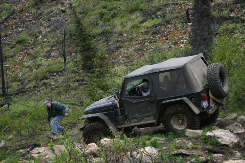 2003 Jeep TJ - A 2003 Jeep TJ tackles a challenging rocky off-road path with a person observing.