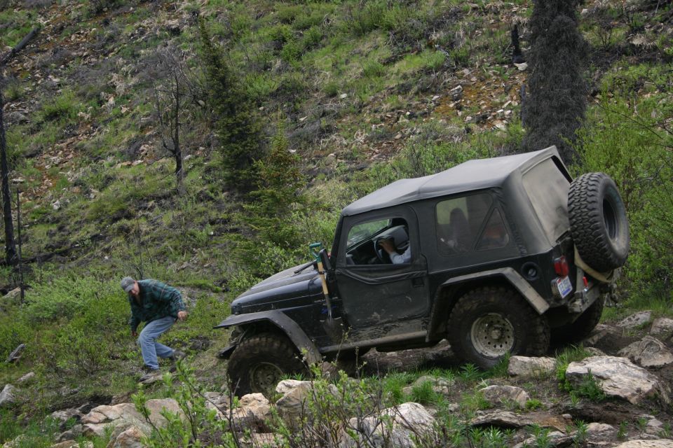 Black 2003 Jeep TJ with soft top navigating a rocky trail, person walking nearby