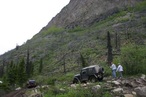 2003 Jeep TJ - Two Jeeps navigate a challenging, rocky trail on a mountainside with sparse vegetation and burnt trees.