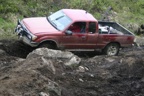 2003 Jeep TJ - A red pickup truck navigates a difficult off-road terrain with muddy obstacles.