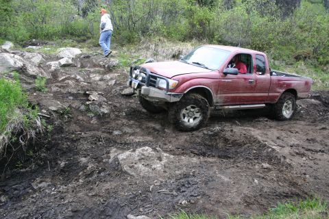 2003 Jeep TJ - Red Toyota Tacoma pickup truck tackling a challenging muddy and rocky off-road course.