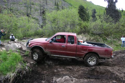 2003 Jeep TJ - A red Toyota Tacoma navigates a challenging off-road trail in a wooded, hilly area.