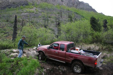 2003 Jeep TJ - A red pickup truck navigates a challenging off-road path in a mountainous, wooded area.