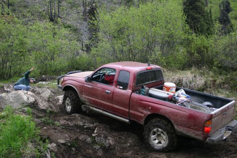 2003 Jeep TJ - A red Toyota Tacoma navigates a challenging off-road trail with a person observing from the side.