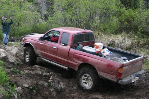 2003 Jeep TJ - Toyota Tacoma pickup truck tackling a challenging off-road course with a driver and passenger.