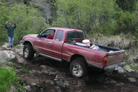 2003 Jeep TJ - A red Toyota Tacoma is shown off-roading on a challenging, rocky terrain.