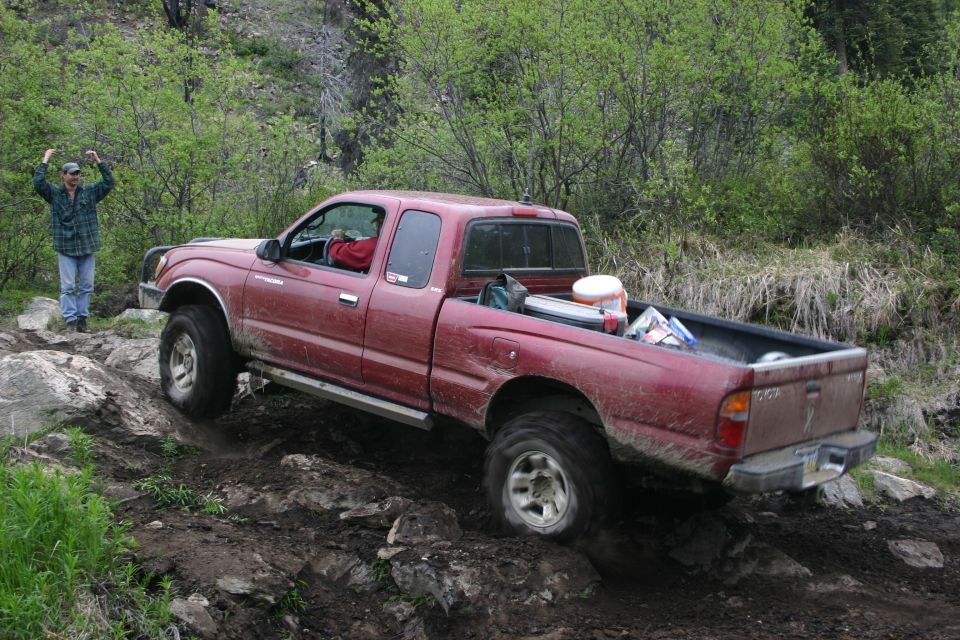 Red Toyota Tacoma pickup truck navigating a rocky trail with a person standing nearby