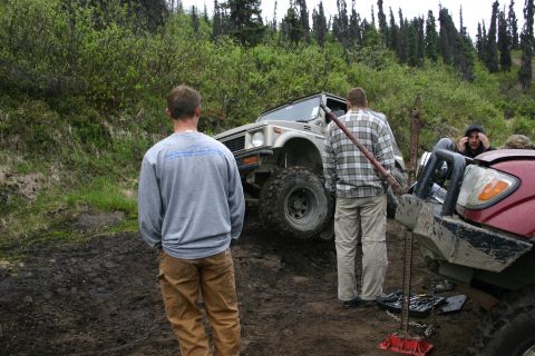 2003 Jeep TJ - Two off-road vehicles are stuck on a muddy trail, with people attempting to free them.