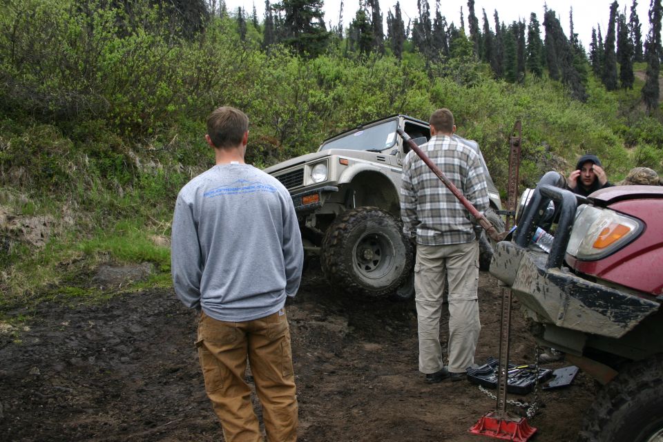 Suzuki Samurai on a muddy incline with a red truck nearby