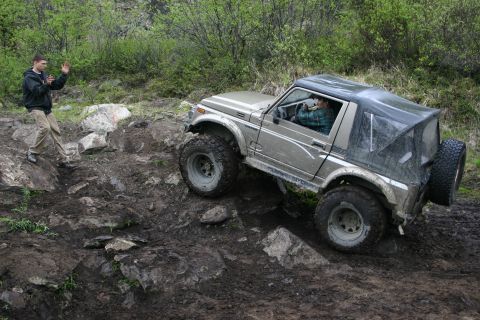 2003 Jeep TJ - A driver maneuvers a Suzuki Samurai over a challenging off-road course with a spotter watching.