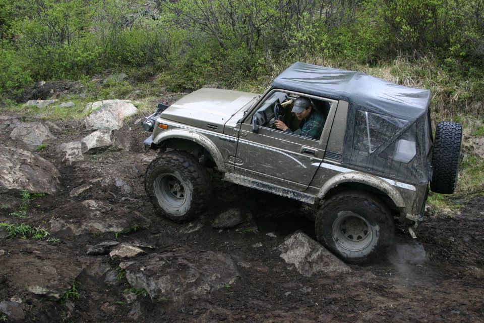 Tan Suzuki Samurai with a soft top navigating a rocky, muddy trail