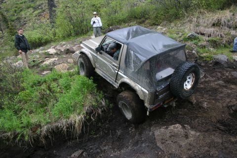 2003 Jeep TJ - Suzuki Samurai tackles a challenging muddy off-road course with spectators observing the action.