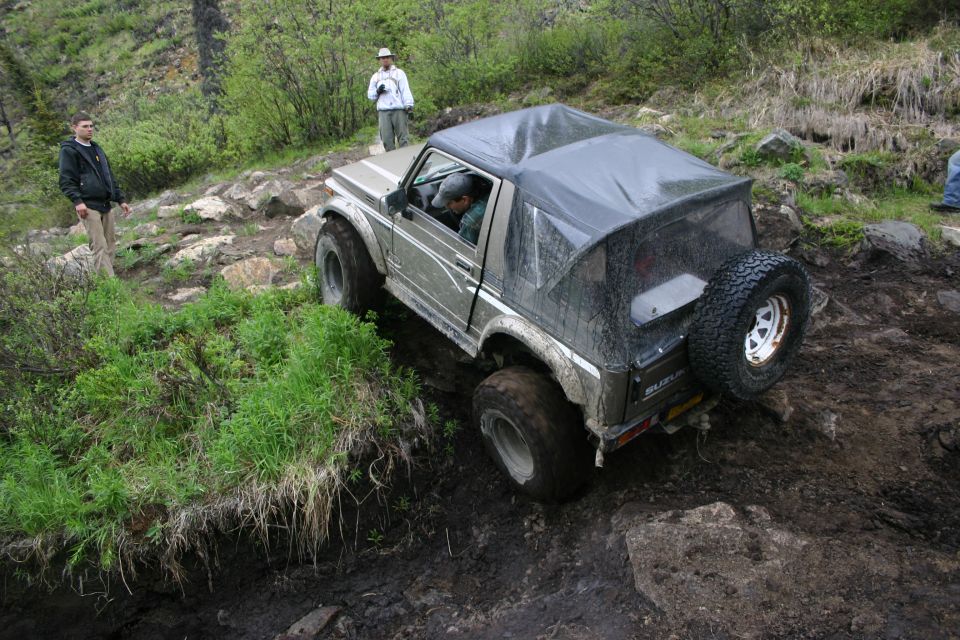 Suzuki Samurai with soft top navigating a muddy off-road trail, two people watching