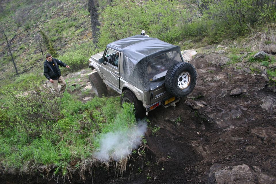Suzuki Samurai climbing a steep, rocky trail with a person watching