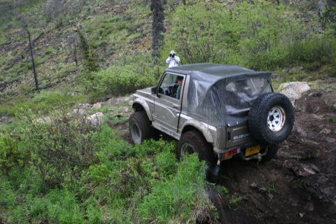 2003 Jeep TJ - A Suzuki Samurai navigates a steep, muddy incline surrounded by lush green foliage.