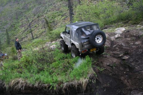 2003 Jeep TJ - A Suzuki Samurai navigates a steep, muddy off-road trail with a person watching from the side.