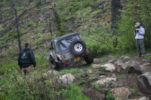 2003 Jeep TJ - A Suzuki Samurai navigates a steep, rocky trail with two onlookers observing the off-road adventure.