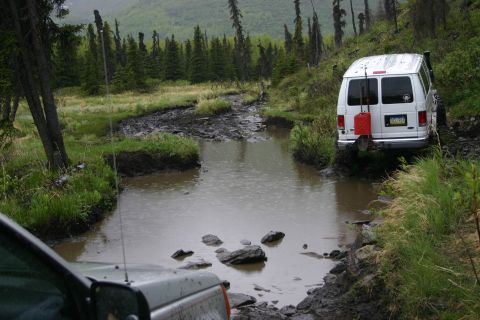 2003 Jeep TJ - Two vehicles traverse a challenging muddy trail with standing water and dense forest.