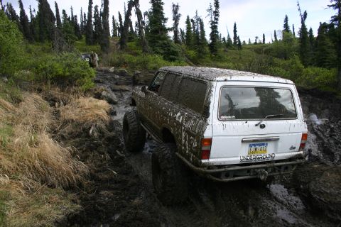 2003 Jeep TJ - A white SUV navigates a challenging muddy and rocky off-road trail.