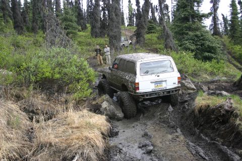 2003 Jeep TJ - White SUV tackles a challenging muddy off-road course with large tires and a modified bumper.