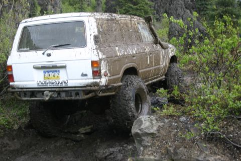 2003 Jeep TJ - Mud-covered Toyota Land Cruiser navigates a rocky, off-road trail.
